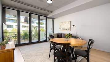 Un intérieur moderne avec une table ronde en bois, des chaises noires, un canapé et une grande fenêtre donnant sur des bâtiments et de la verdure.