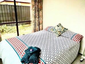 Un lit avec une literie et des oreillers à motifs, une fenêtre avec des rideaux et une vue sur l’extérieur.