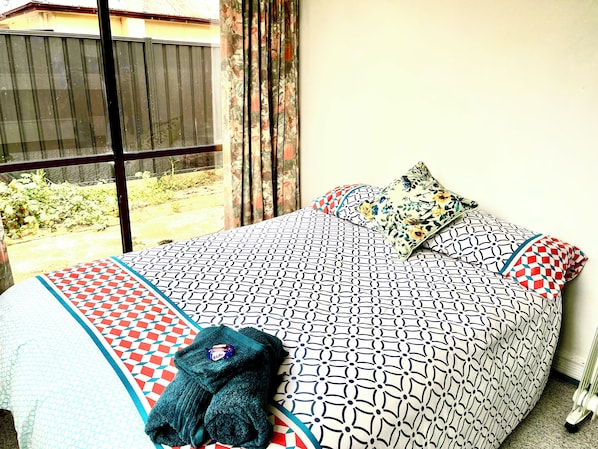 A bed with patterned bedding and pillows, a window with curtains, and a view of the outdoors.