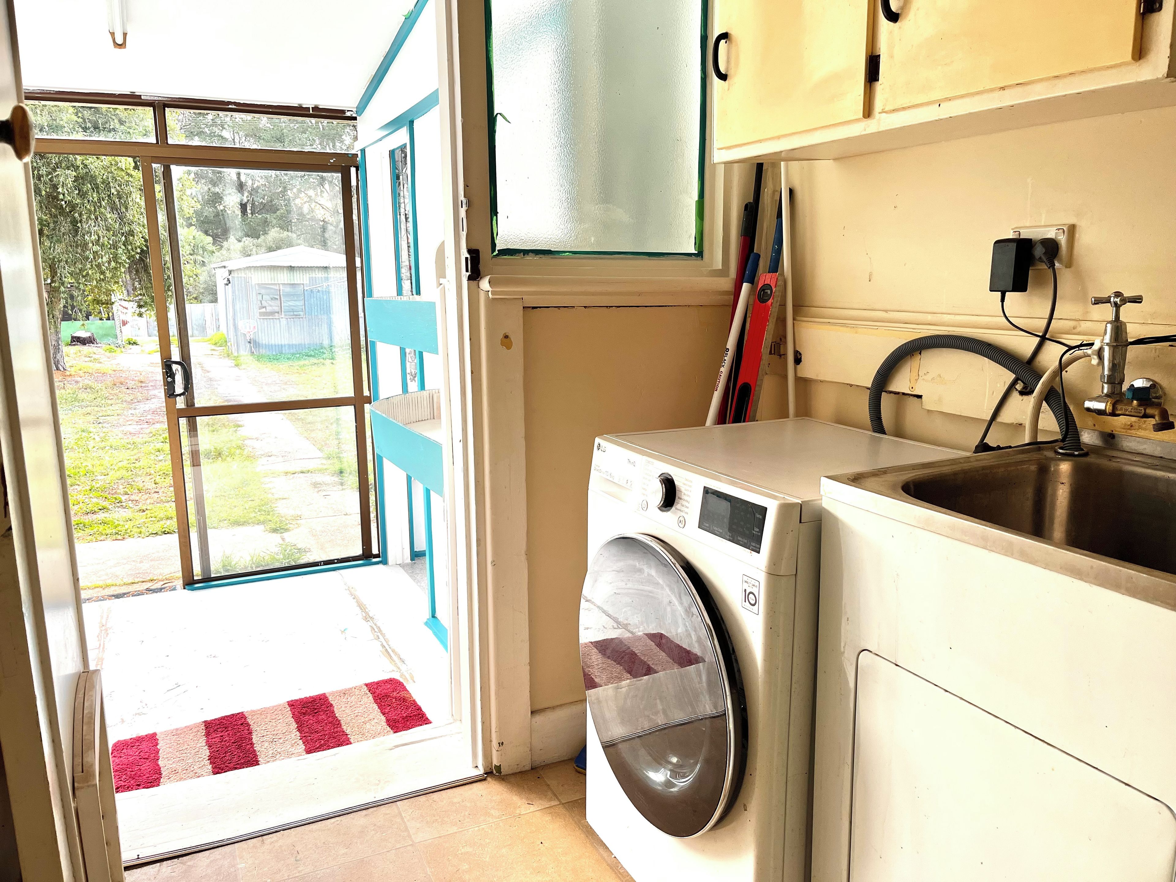 Een wasruimte met een wasmachine, een spoelbak en een deur naar een tuin.