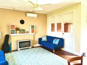 A room with a blue sofa, a patterned rug, a ceiling fan, and a fireplace.