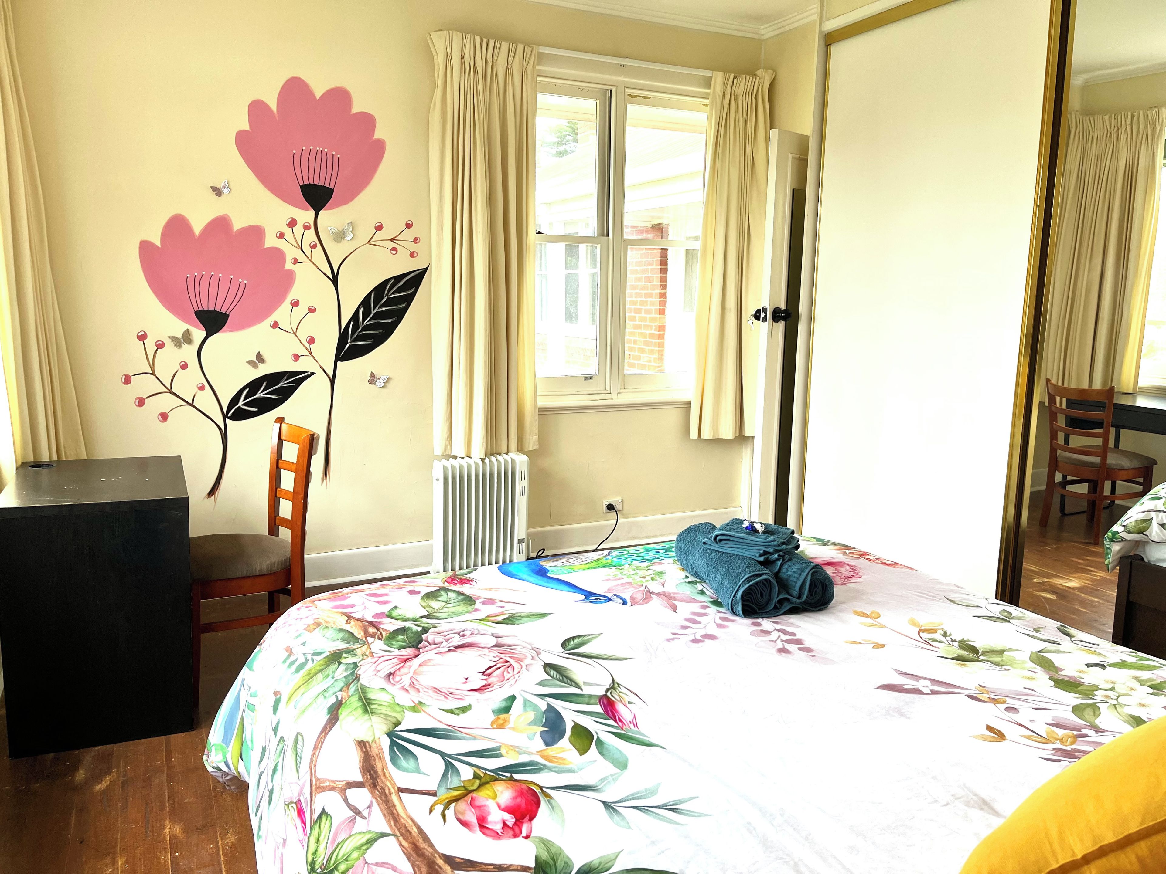 Een slaapkamer met een bed, een radiator, een stoel, een bureau en een raam met gordijnen.