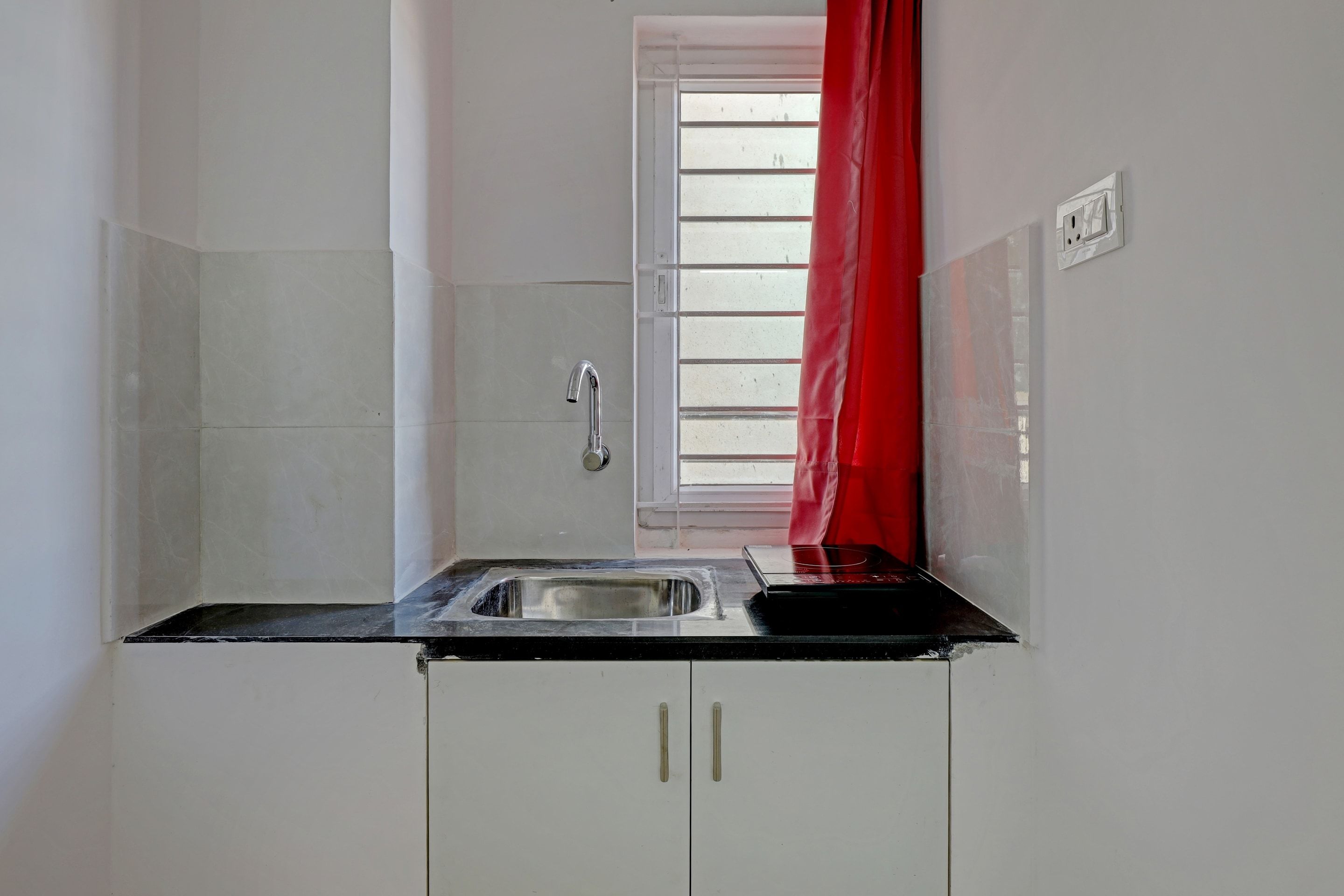A kitchen with white cabinets, a stainless steel sink, and a window with blinds.