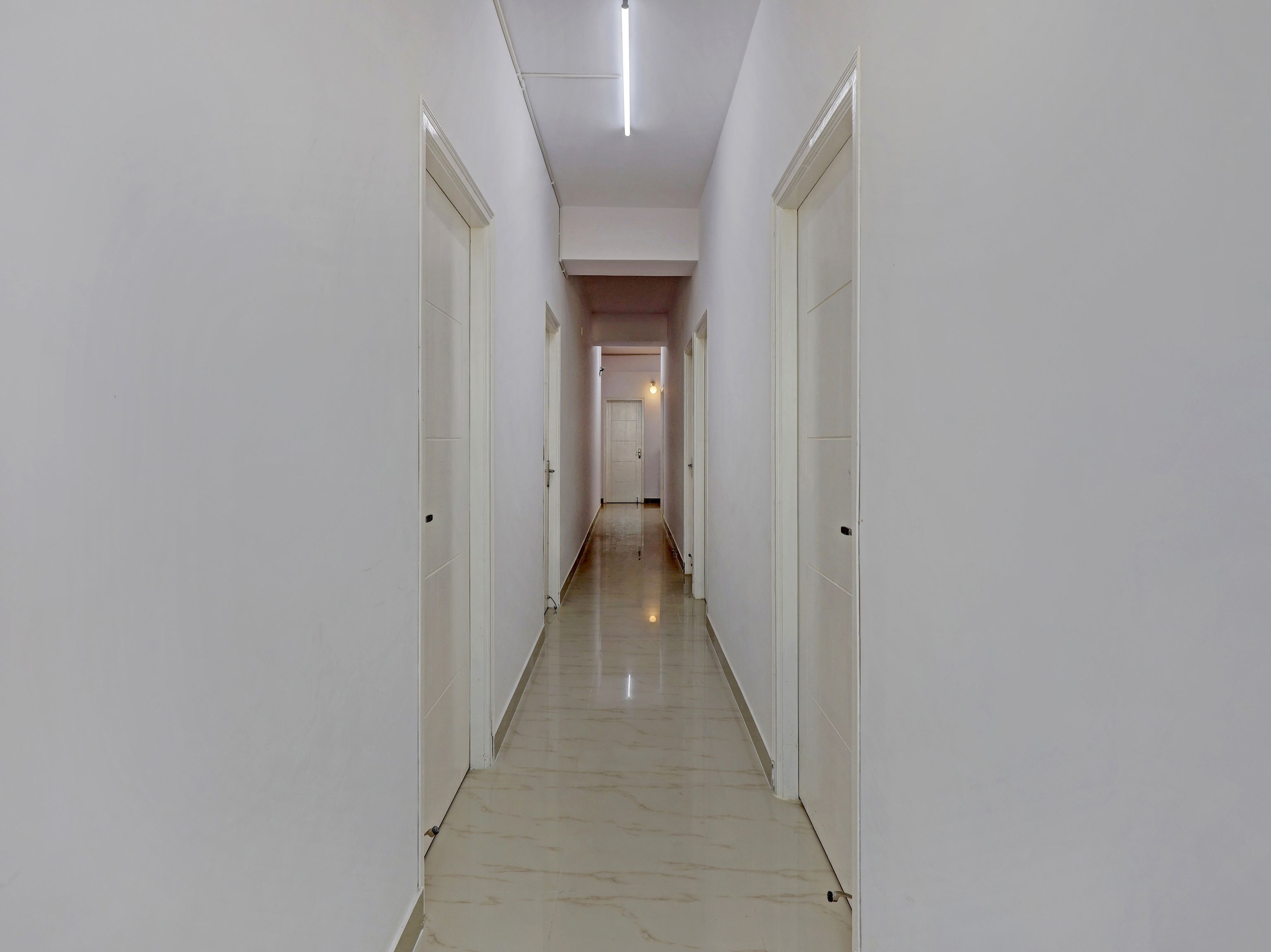 A corridor with white walls and doors, leading to a room with a door at the end.