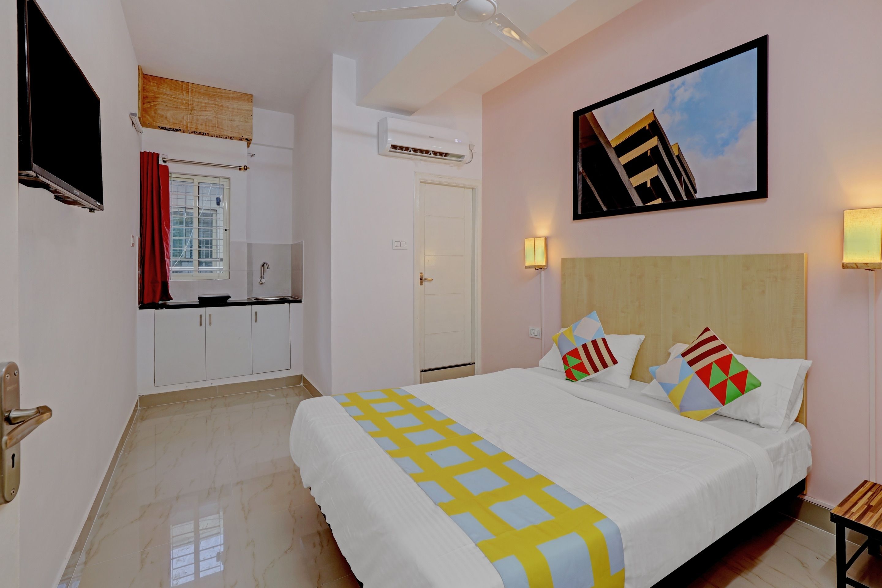 A hotel room with a bed, a TV, a window with curtains, a door, and a ceiling fan.