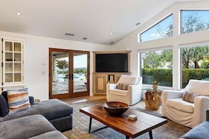 Uma sala de estar moderna com uma televisão grande, assentos confortáveis e vista para o exterior.