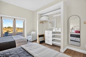 Ein Schlafzimmer mit zwei Betten, einem begehbaren Kleiderschrank, einem großen Spiegel und Blick ins Freie.
