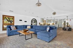 A spacious living room with a sectional sofa, a coffee table, and a large window with a view of trees. - Pool + Hot Tub | Fire Pit + Hammock | Hilltop Valley Views | Vino Vista Villa (Paso Robles)