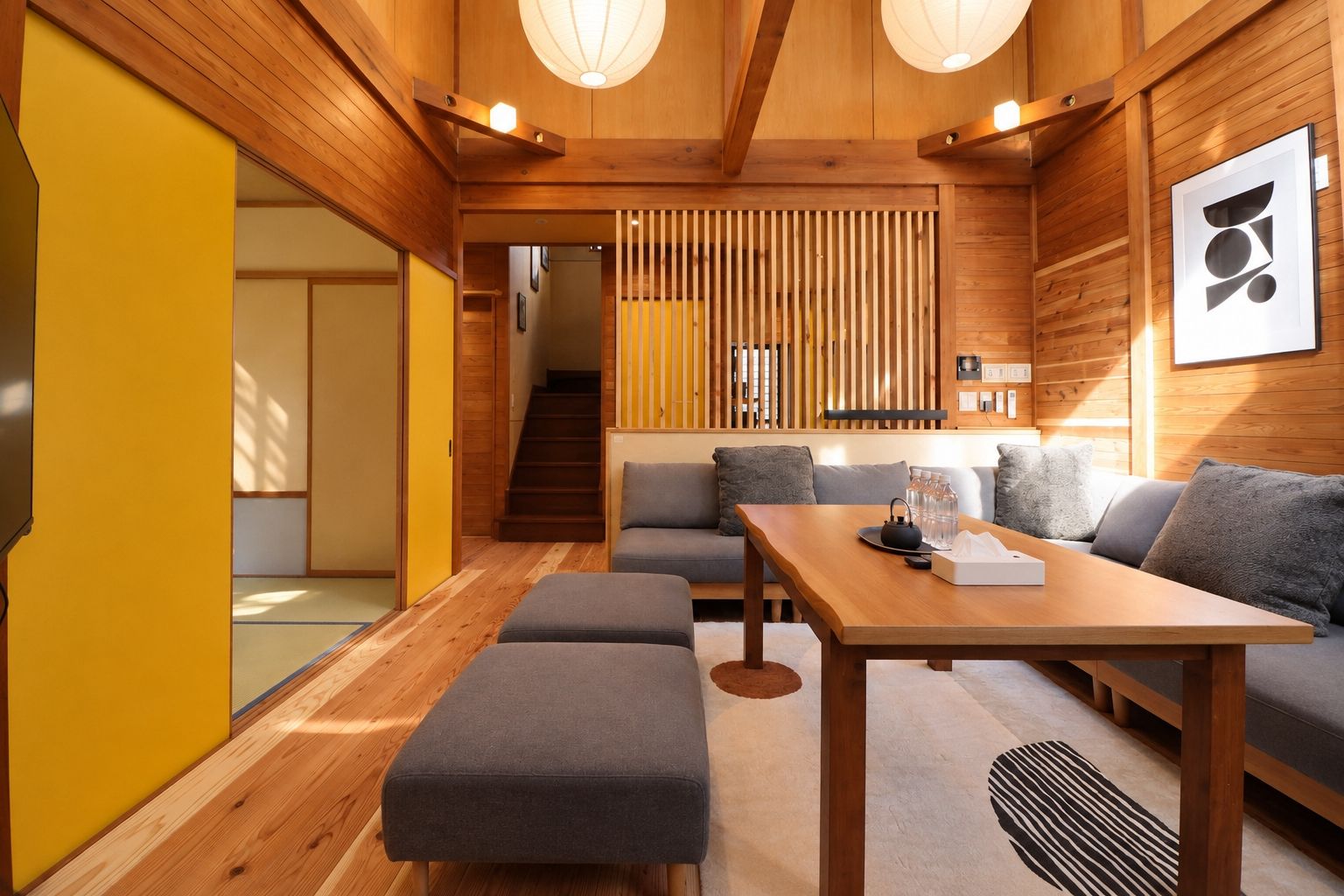 Ein modernes Interieur mit Holzboden, einer Sofagarnitur, einem Esstisch und einer Treppe, die in einen weiteren Raum führt.