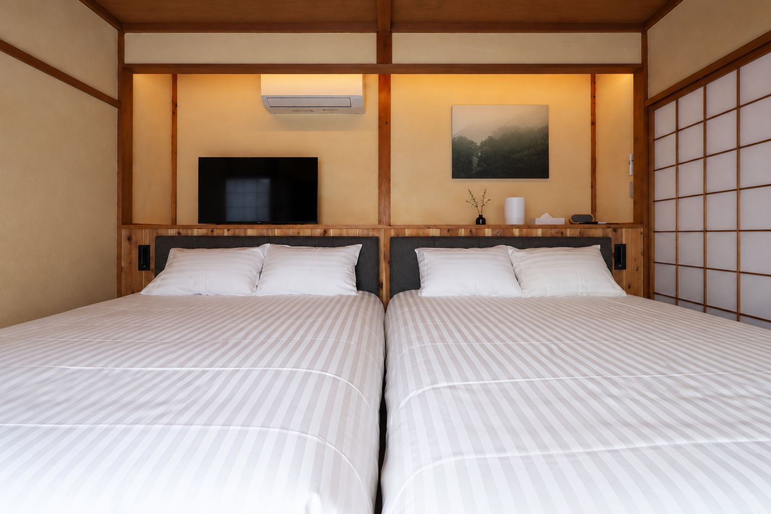Habitación de hotel con dos camas, un televisor, un cuadro y una puerta corredera tradicional al estilo japonés.
