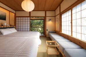 A traditional Japanese-style bedroom with tatami flooring, a large bed, a low wooden bench, and a sliding door leading to a garden.