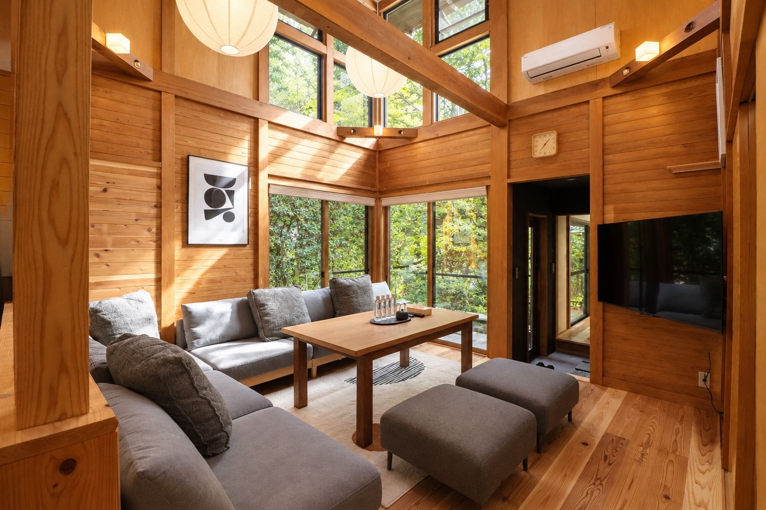 Un interior moderno con suelo de madera, un conjunto de sofás, una mesa y un televisor montado en la pared.