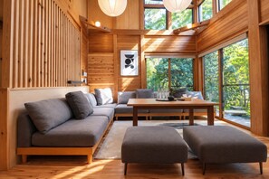 Un interior moderno con un muro de listones de madera, un sofá gris, una mesa de madera y ventanas amplias con vistas a zonas verdes.