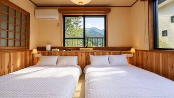 A room with two beds, a window with a view of mountains, a wooden headboard, and a wall-mounted air conditioner.