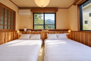 Habitació amb dos llits, una finestra amb vista a muntanyes, un capçal de llit de fusta i un aire condicionat fixat a la paret.