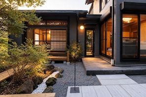 Edifici modern amb interior japonès tradicional, un jardí ben cuidat amb roques i plantes, i un camí clar que condueix a l'entrada.