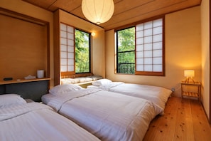 A traditional Japanese-style room with tatami flooring, a low wooden ceiling, and sliding shoji screens. There are two beds with white bedding and a small bedside table with a lamp. - KihadaNikko (Nikko)