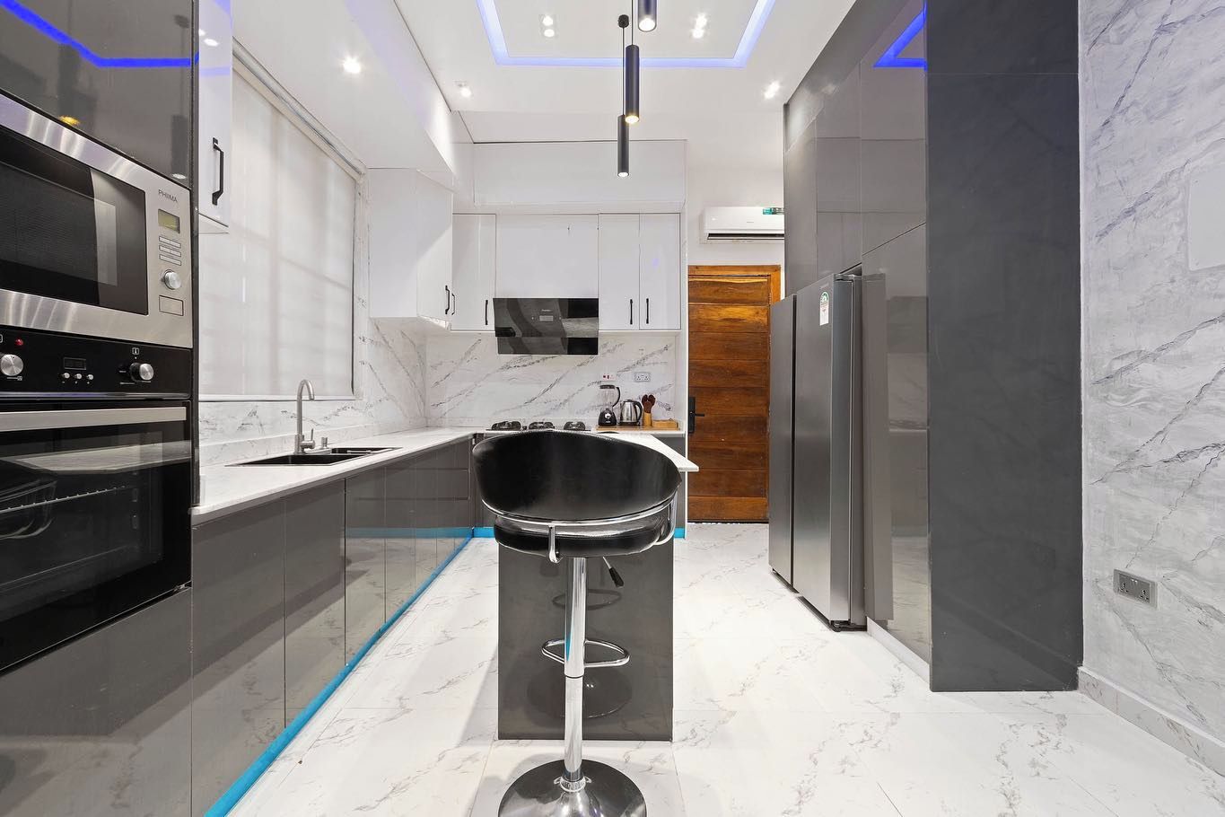 Una cocina moderna con horno empotrado, microondas, pileta y un taburete de bar.