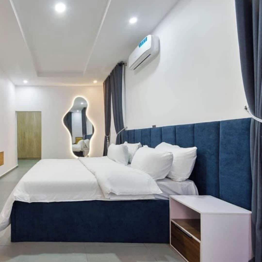 A modern hotel room with a large bed, a bedside table, and a built-in air conditioning unit.