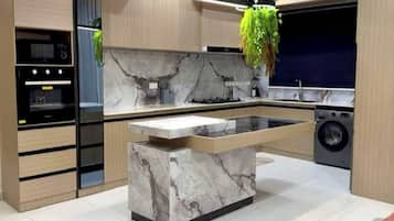 A modern kitchen with a marble island, built-in appliances, and a hanging plant.