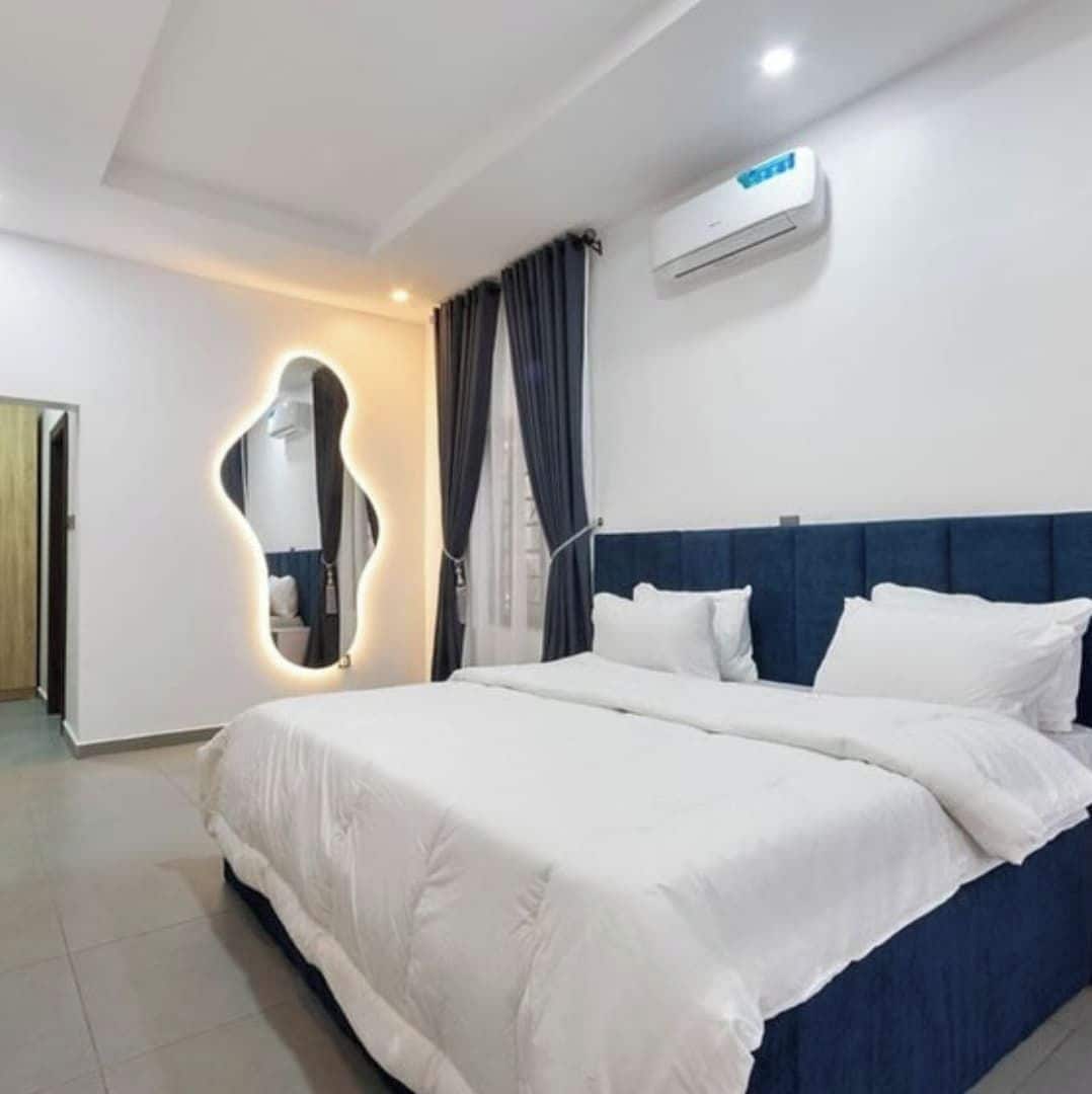 Une chambre d’hôtel avec un grand lit, un miroir doté d’un cadre original, un climatiseur fixé au plafond et une porte située à gauche.