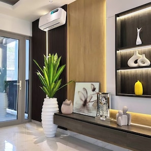 A modern interior with a large potted plant, a framed picture, and decorative items on a shelf.