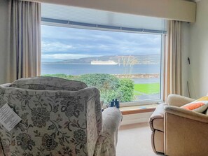 A room with a large window offering a view of the sea and distant hills. There are two chairs with floral upholstery. - 3 bedroom accommodation in Wemyss Bay (Wemyss Bay)