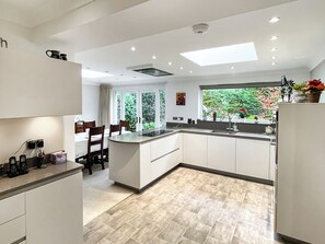 A modern kitchen with a central island, a dining area with chairs, and a view of greenery outside. - 3 bedroom accommodation in Wemyss Bay (Wemyss Bay)