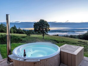 A hot tub with a bottle of wine and glasses, surrounded by a wooden deck, overlooking a lake and distant mountains. - Fairlie Ward Cottage (Fairlie)