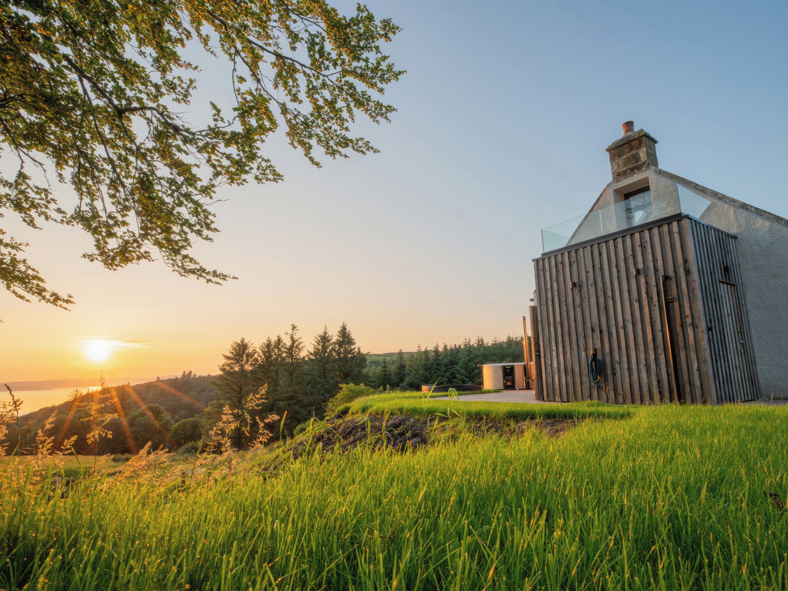 A rustic barn with a sloped roof and a chimney, surrounded by lush green grass and trees.