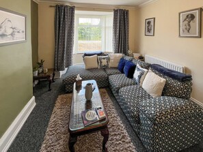 A living room with a patterned sofa, a glass coffee table, and a window with curtains. - 2 bedroom accommodation in Fir Tree, near Bishop Auckland (Fir Tree, near Bishop Auckland)