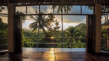 Una habitación con un amplio ventanal que da a un paisaje exuberante con palmeras y una montaña.