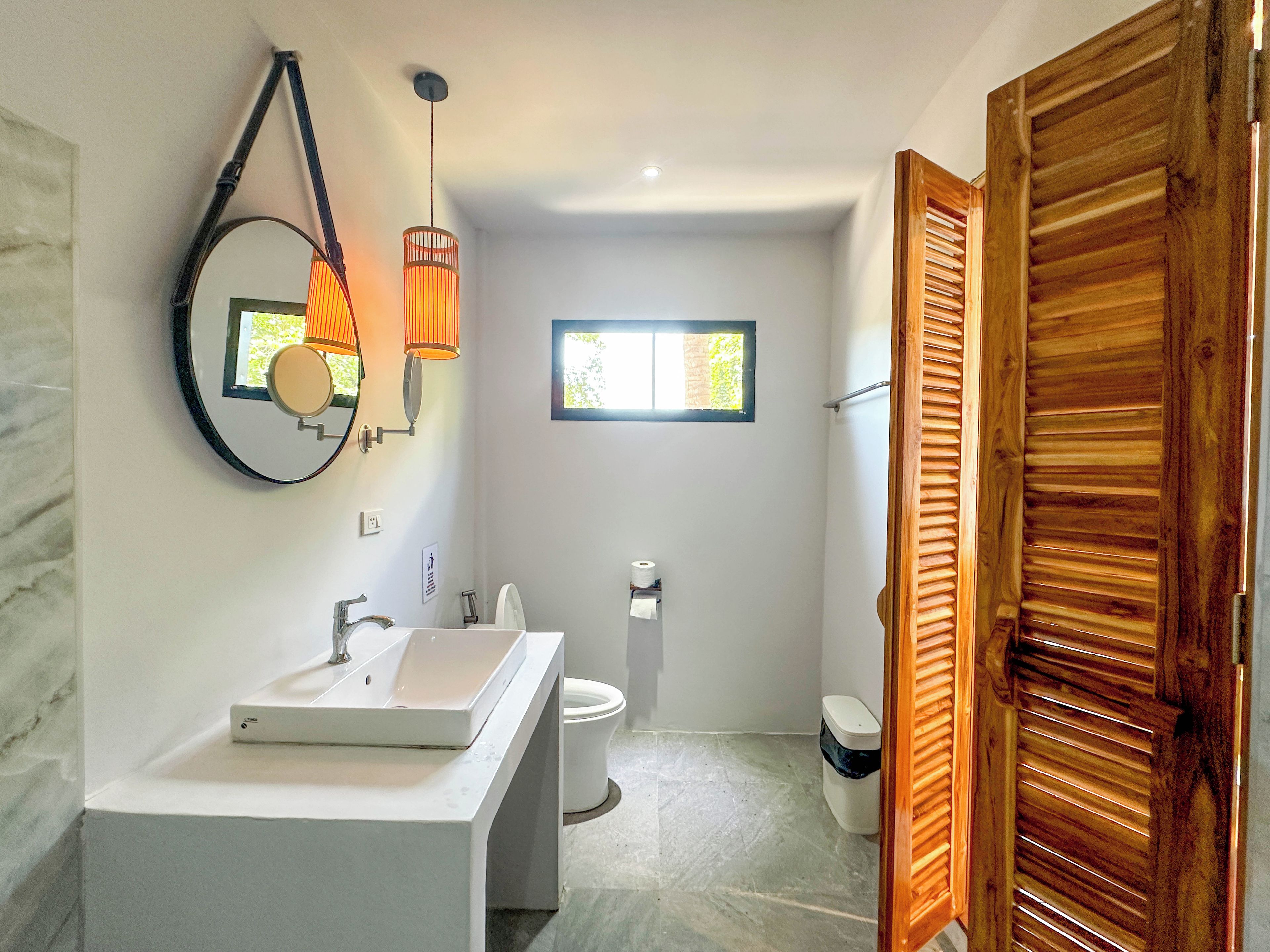 A modern bathroom with a large mirror, two sinks, a toilet, and a window.