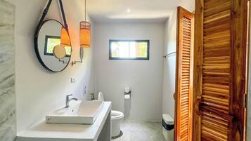 A modern bathroom with a large mirror, two sinks, a toilet, and a window.