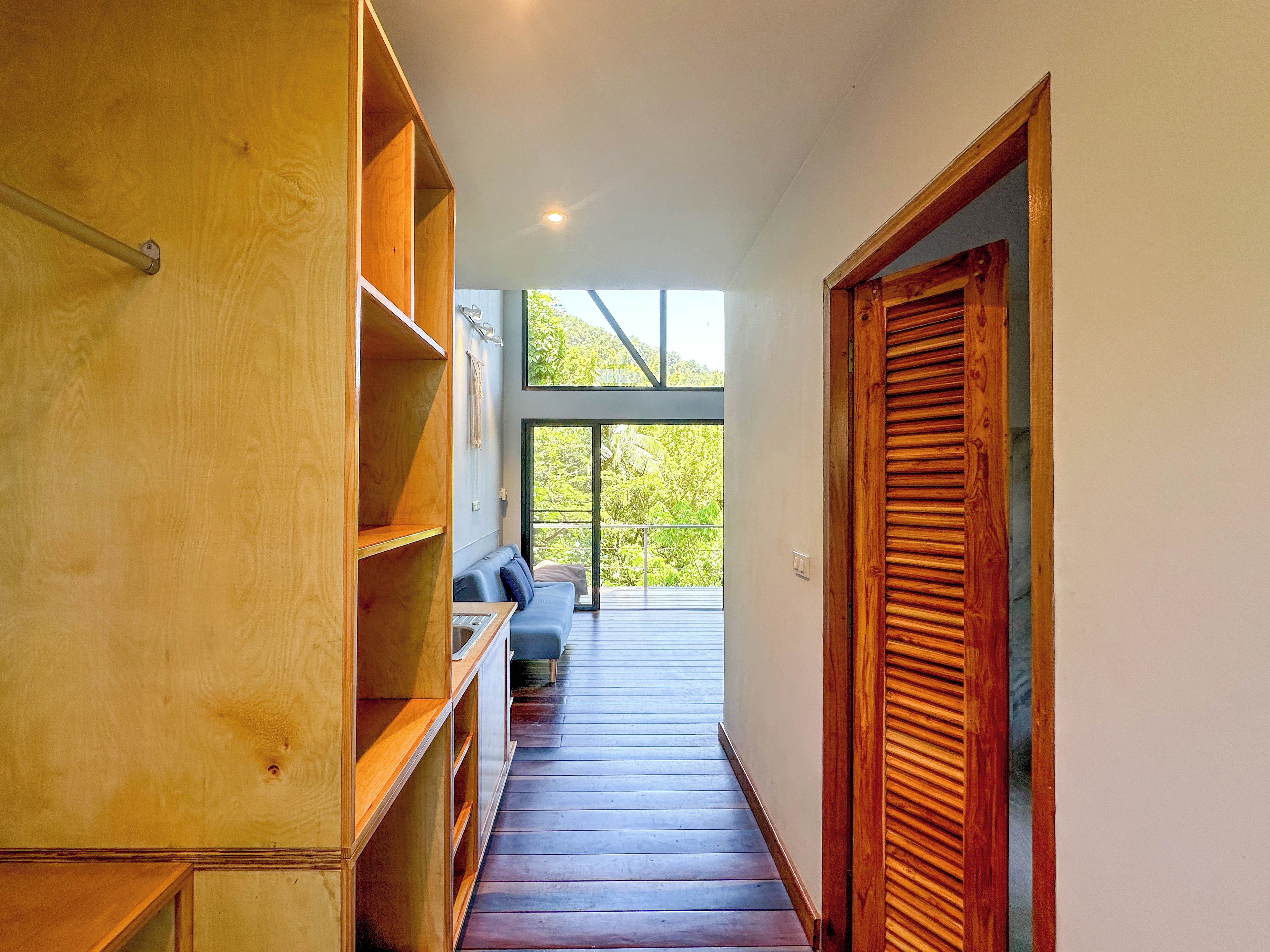 Un pasillo de madera con estanterías empotradas, un banco y vistas al exterior con vegetación.