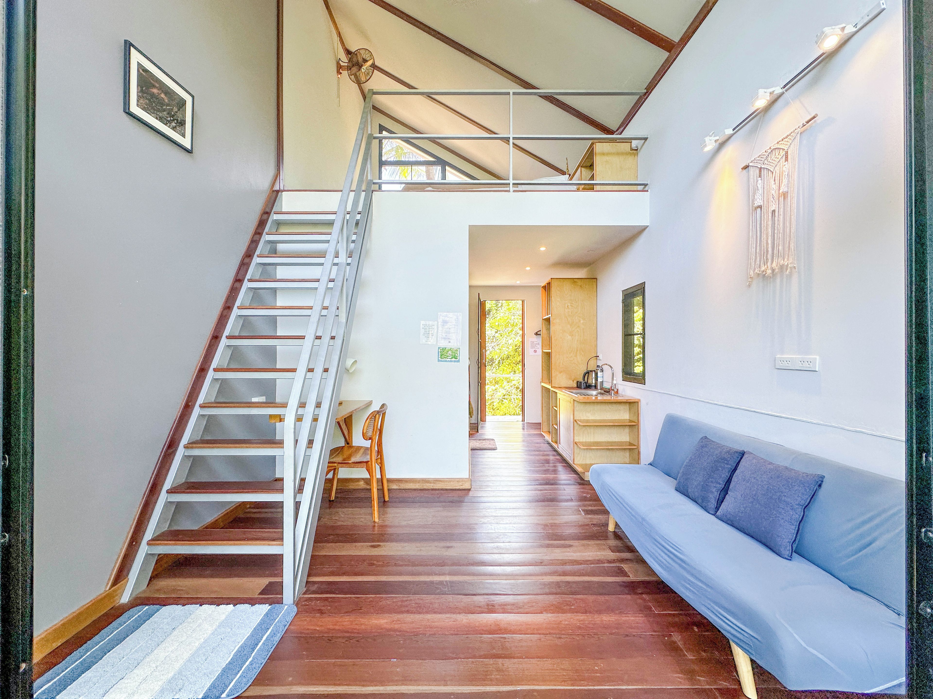 Una escalera que conduce a un nivel superior, un sofá azul y una pequeña zona de kitchenette.