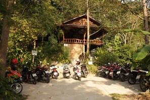 Una fila de motocicletas estacionadas frente a una estructura de madera con balcón, rodeada de abundante vegetación.