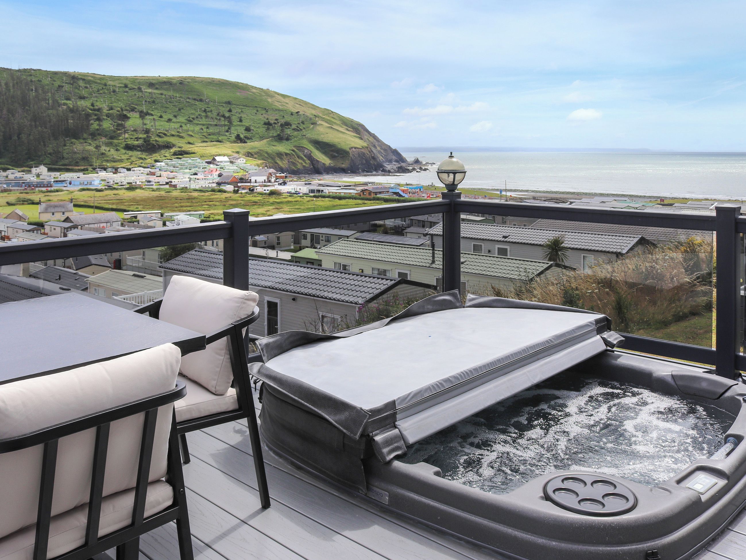 A balcony with a hot tub, outdoor seating, and a view of a coastal village.