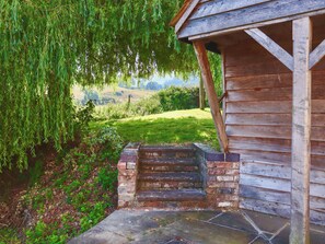 A wooden building with a stone staircase leading to a porch, surrounded by lush greenery and a view of rolling hills. - 4 bedroom accommodation in Coaley (Coaley)