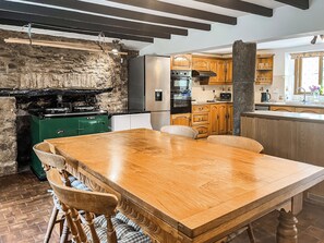 A kitchen with a wooden table, chairs, a green stove, and wooden cabinets. - 4 bedroom accommodation in Bickington (Bickington)