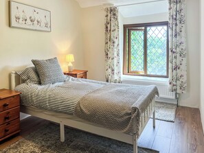 A bedroom with a bed, a nightstand, a lamp, a dresser, and a window with curtains. - 4 bedroom accommodation in Bickington (Bickington)