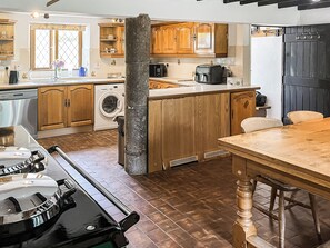 A kitchen with wooden cabinets, a washing machine, and a dining area with a table and chairs. - 4 bedroom accommodation in Bickington (Bickington)