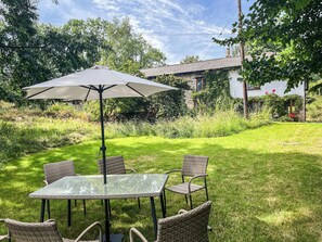 A glass-top table with four wicker chairs and a large umbrella in a grassy backyard with a house in the background. - 4 bedroom accommodation in Bickington (Bickington)