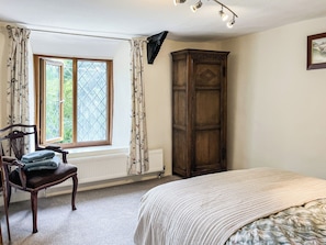 A bedroom with a bed, a chair, a wardrobe, a window with curtains, and a radiator. - 4 bedroom accommodation in Bickington (Bickington)