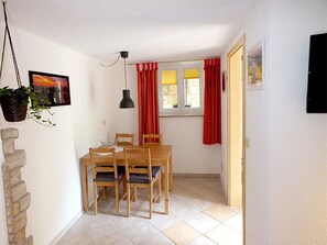 A dining area with a table and chairs, a hanging plant, a pendant light, and a window with red curtains. - Holiday Apartment in Altendorf With Wi-fi (Sebnitz)