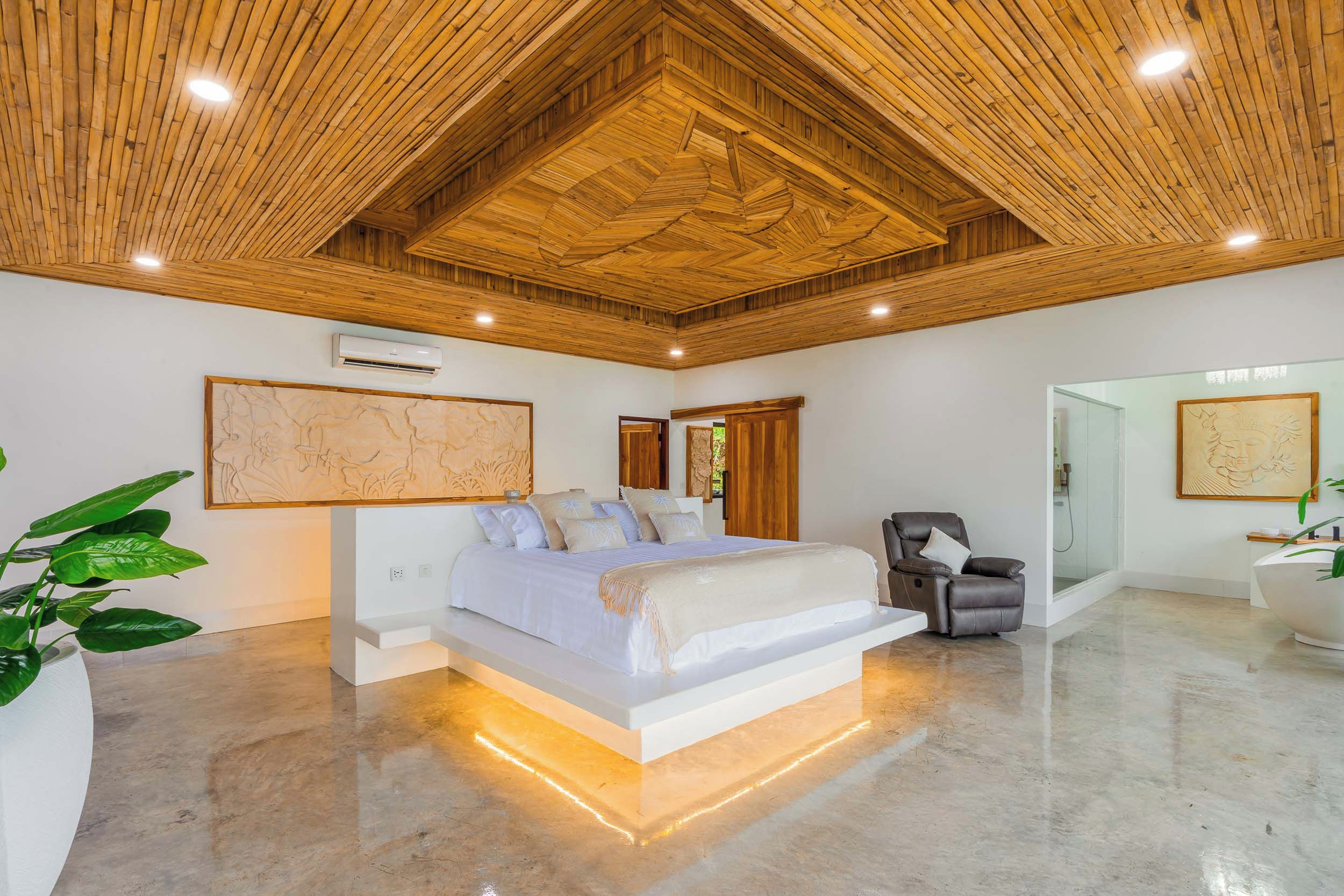 A modern bedroom with a large bed, a wooden ceiling, and a glass shower area.