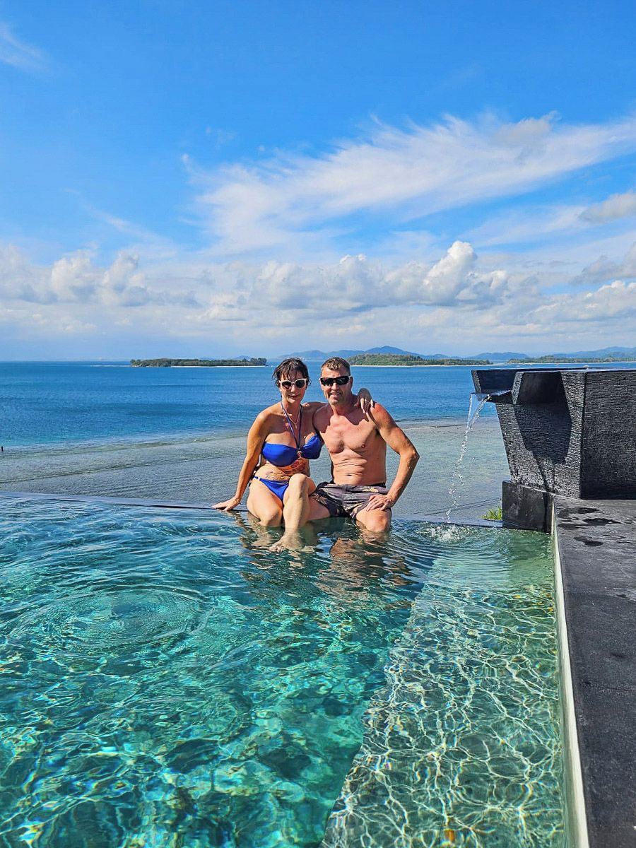 Una pareja sentada en una piscina transparente con vistas al mar y a islas distantes.