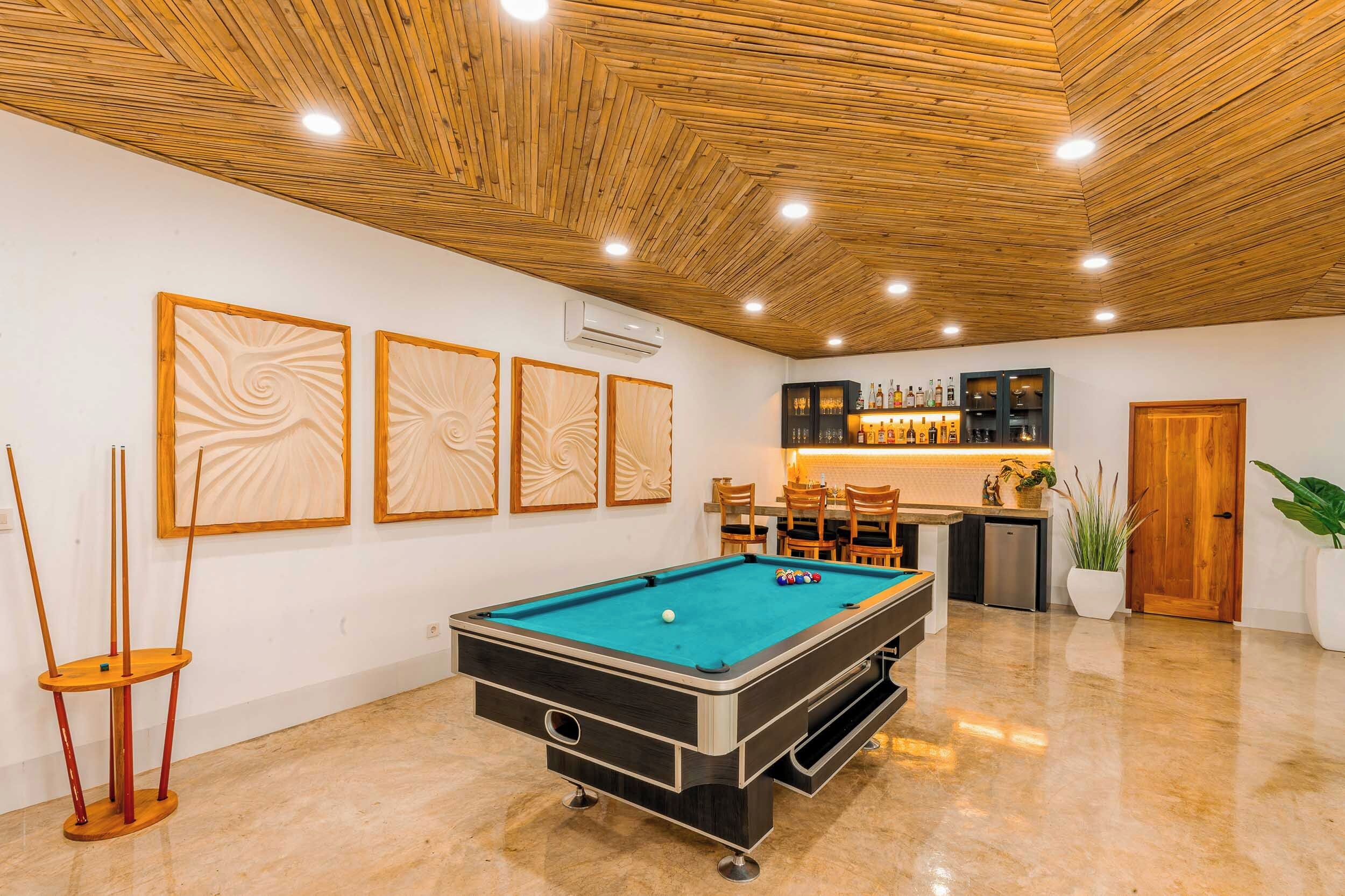 A pool table with a billiard cue and balls, a bar area with bottles, and a wooden ceiling.