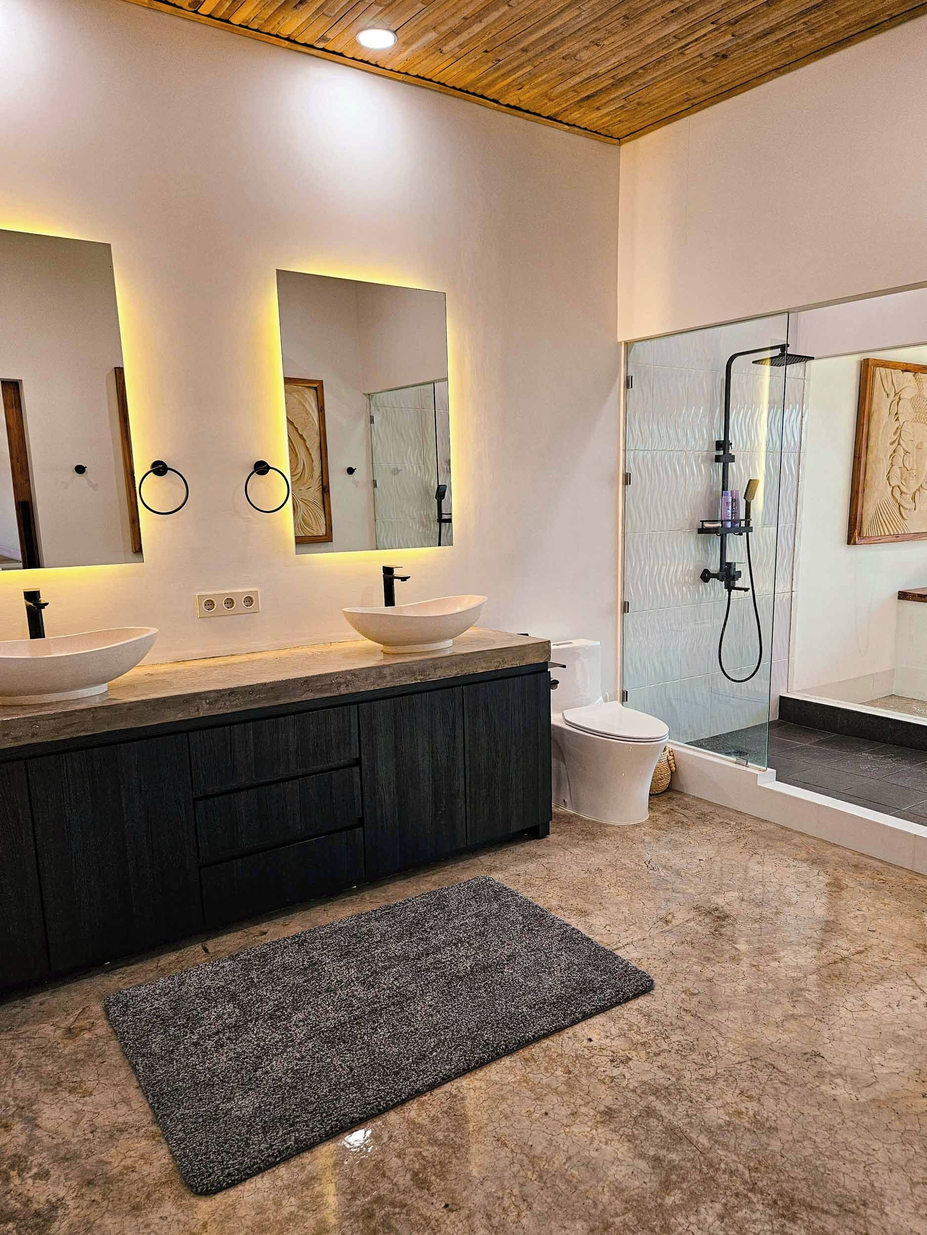 A modern bathroom with two sinks, a shower, and a large mirror.