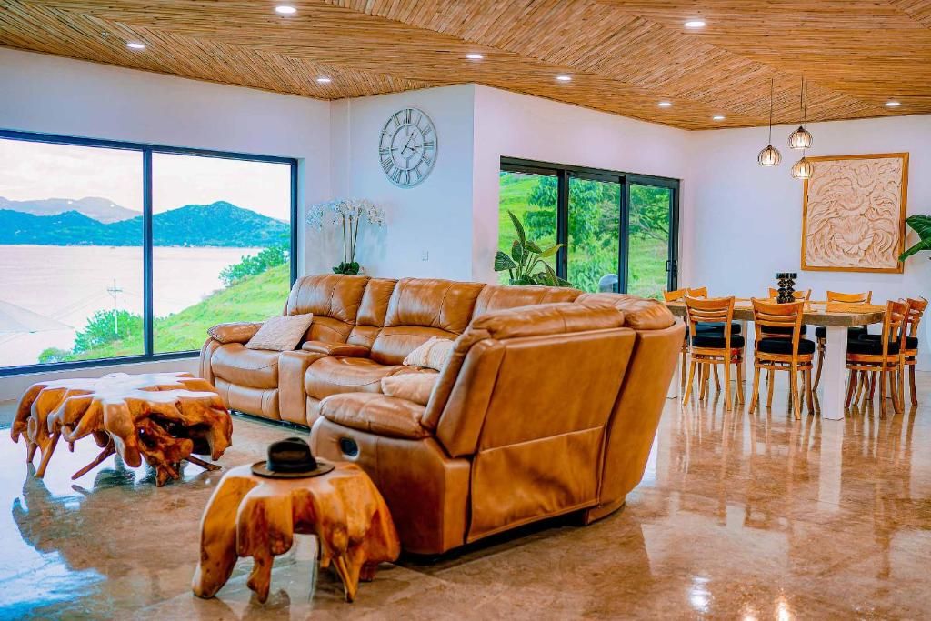 Un vaste espace de vie comprenant un canapé en cuir, une table à manger, des chaises et une grande fenêtre donnant sur un lac et des montagnes.